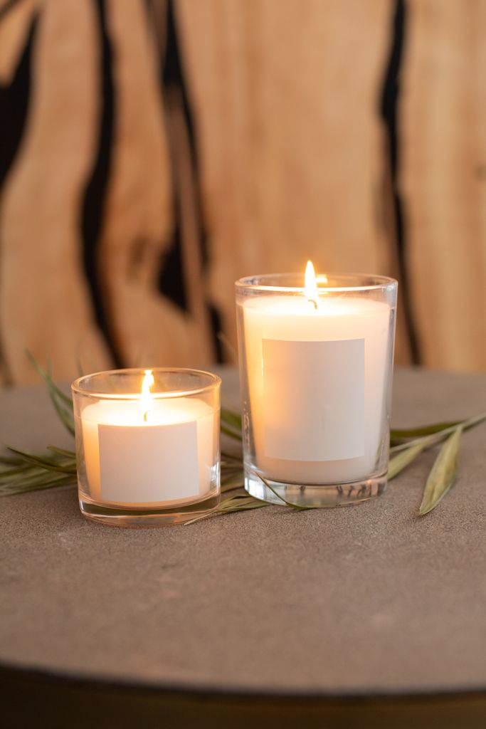 Two lighted candles in clear glass holders on a table with leaves - perfect for a cozy ambiance.